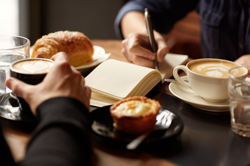 Table with coffee, pastries and one person taking notes